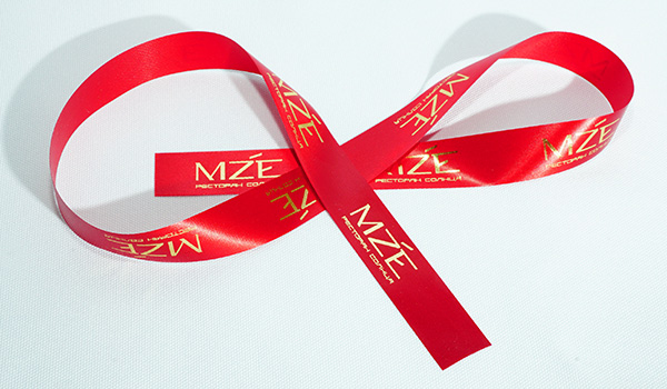 Ярко-красная сатиновая лента с золотыми логотипами, сложена в виде банта