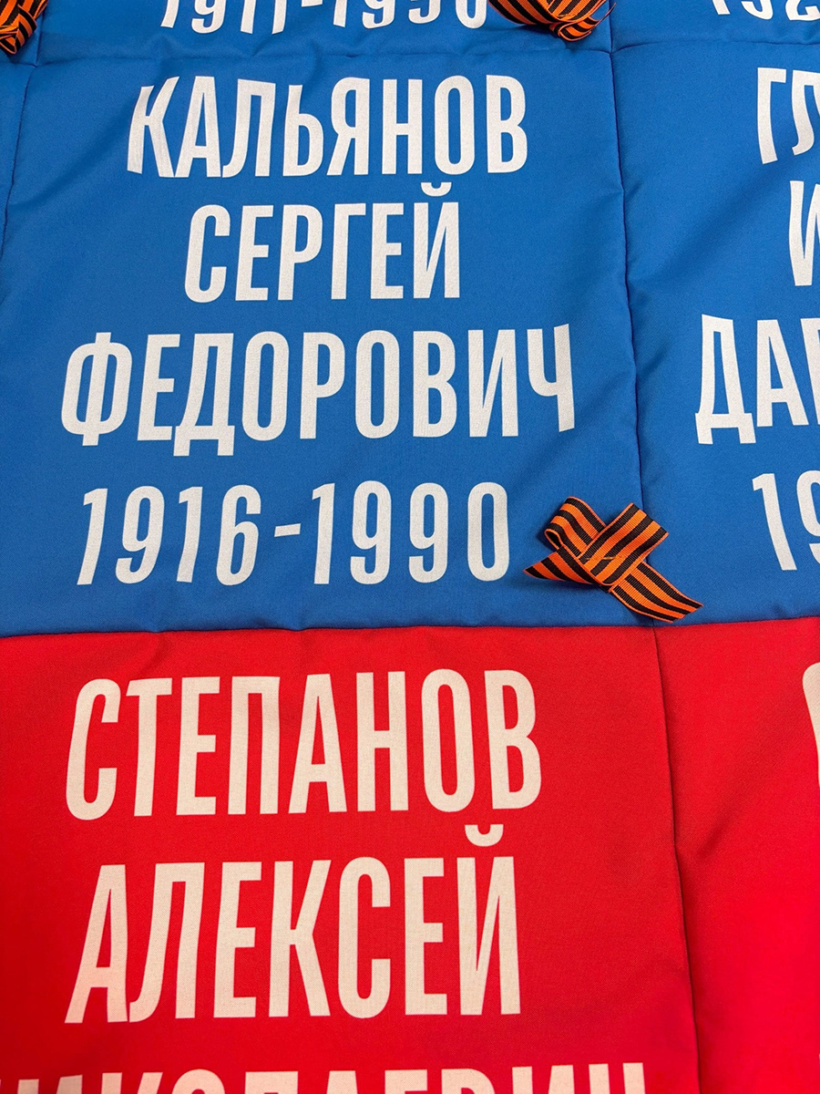 Сшитые синие и красные полотна ткани с белыми именами, фамилиями и георгиевскими бантами