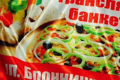 Яркий отпечаток рекламного баннера с красными надписями и фото пиццы на атласной ткани