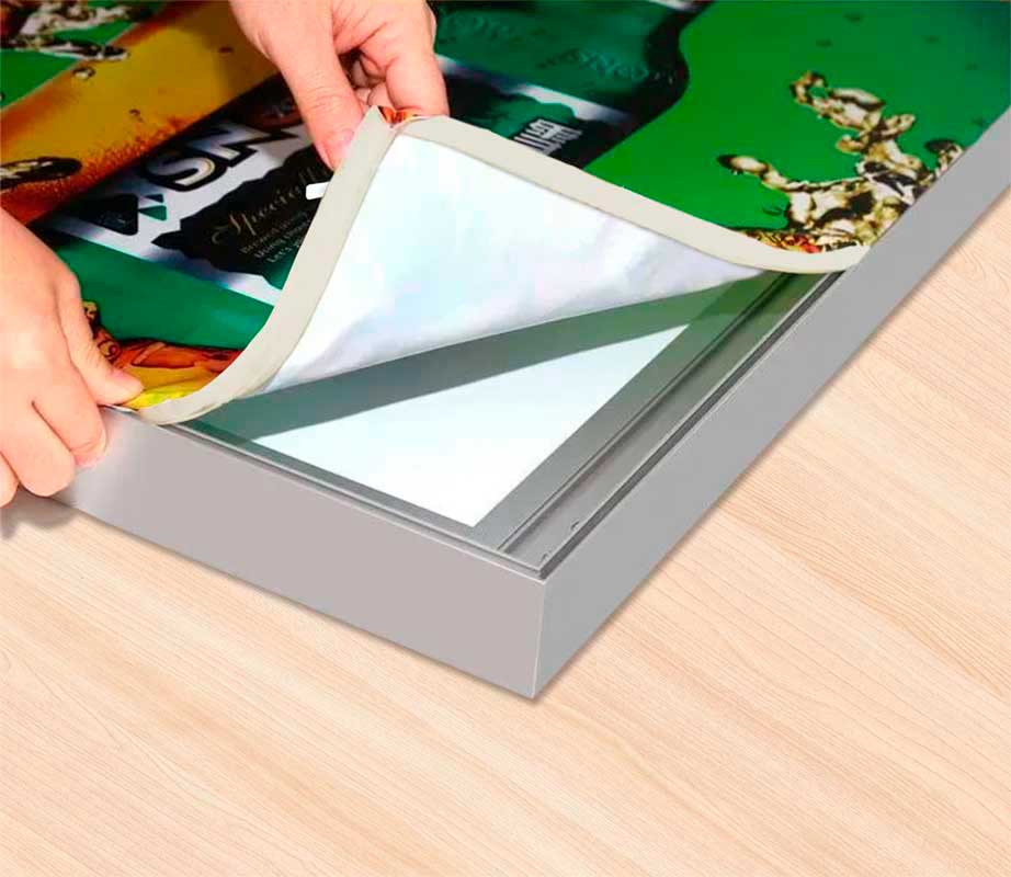 Вид угла светового короба с руками, заправляющими полотно в пазы.